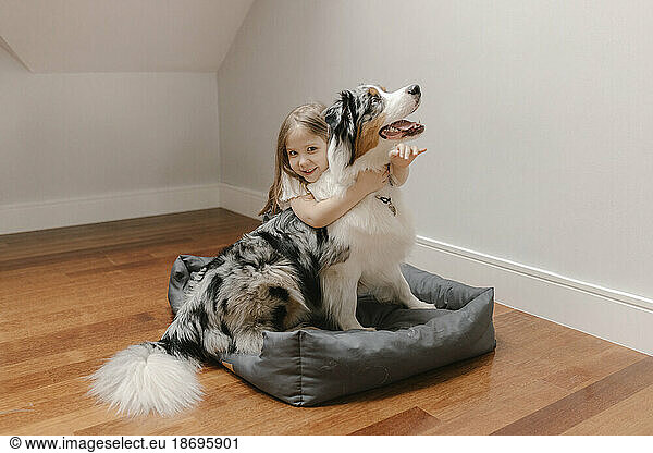Girl embracing Australian Shepherd on pet bed at home