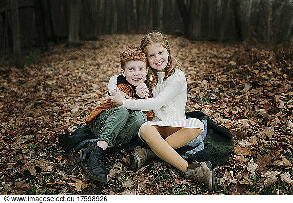 Girl embracing brother sitting on autumn leaves
