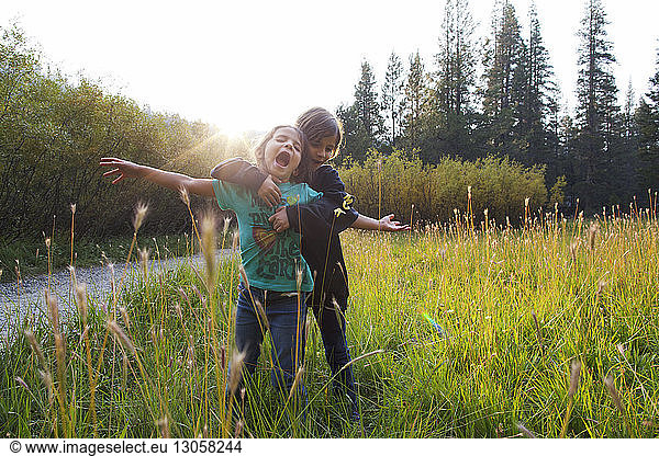 Girl embracing friend while standing on grass against sky