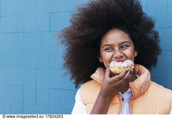 Girl enjoying doughnut in front of blue wall