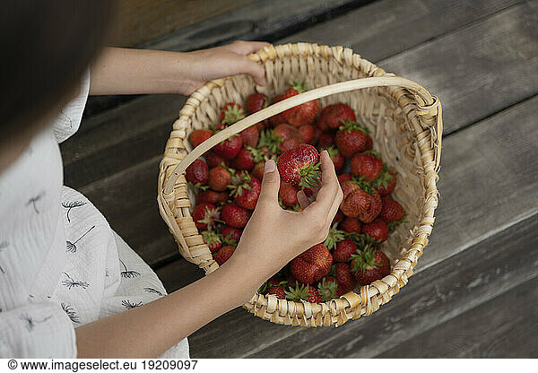 Girl examining strawberry from basket