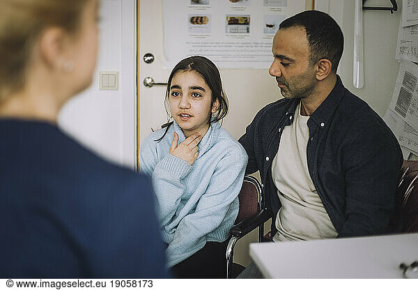 Girl explaining illness to nurse while sitting next to father in clinic