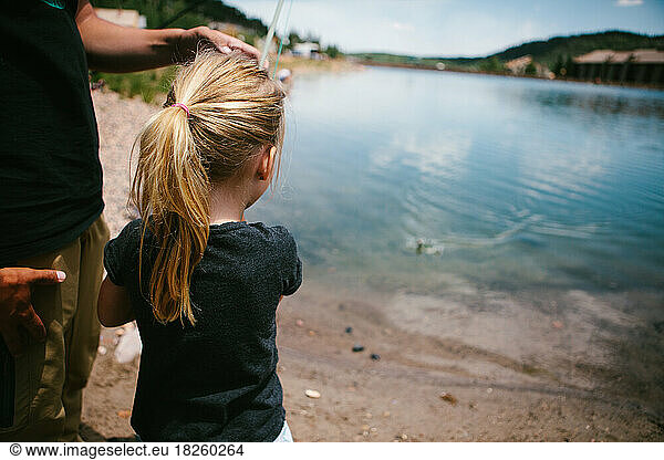Girl fishes with a fishing pole at a mountain pond on vacation