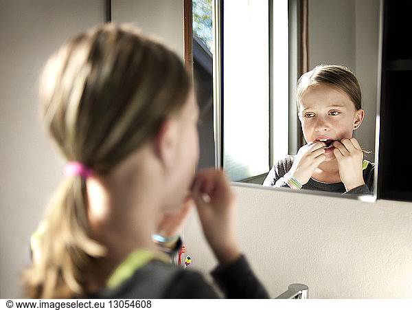 Girl flossing teeth in bathroom seen through mirror