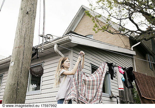 Girl hanging clothes on rope outside house