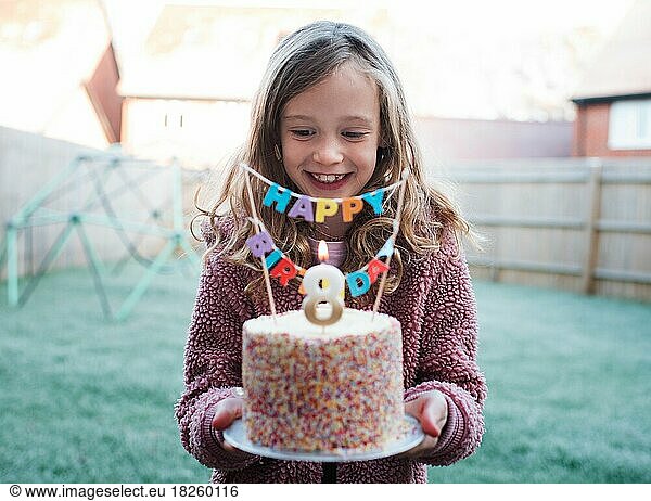 girl happily holding a 8th birthday cake on her birthday