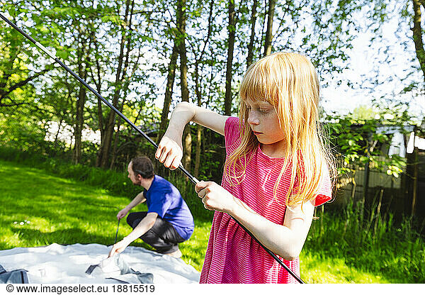 Girl helping father to prepare tent for camping