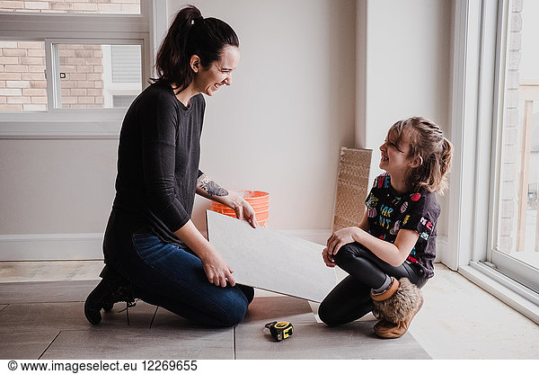 Girl helping mother installing floor tiles