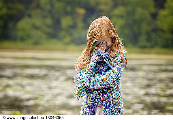 Girl hiding face with hand while standing against lake
