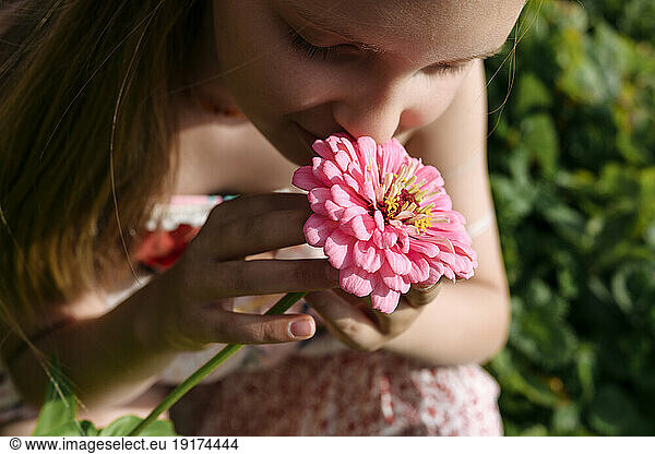 Girl holding and smelling pink flower in garden
