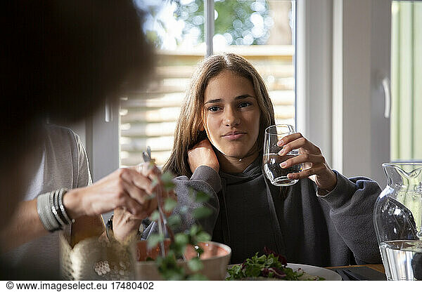 Girl holding drinking glass while having food with mother at home