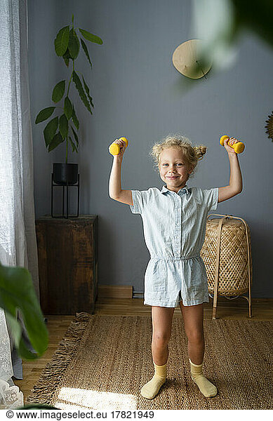 Girl holding dumbbells standing at home