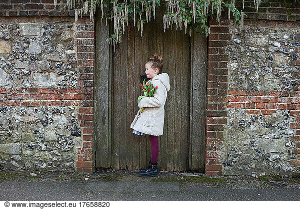 girl holding flowers stood by an old English door