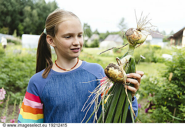 Girl holding freshly harvested onions in garden