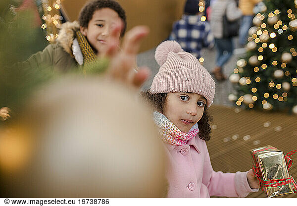 Girl holding gift box with brother enjoying at Christmas market