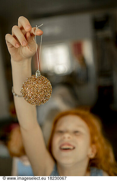 Girl holding glitter Christmas bauble at home