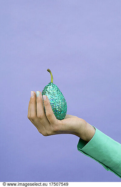 Girl holding glittered pear by lavender background