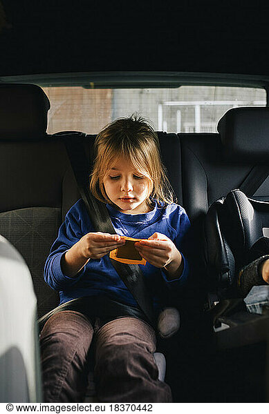 Girl holding playing card sitting at back seat in car