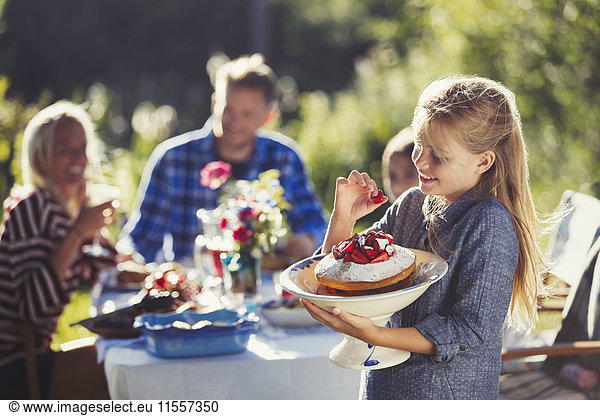 Girl holding strawberry cake at sunny garden party patio table