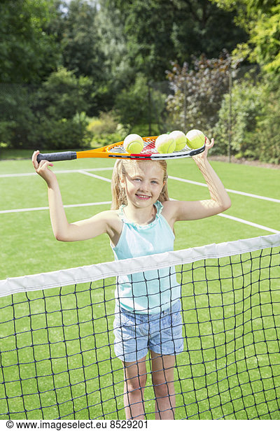 Girl holding tennis racket and balls on grass court