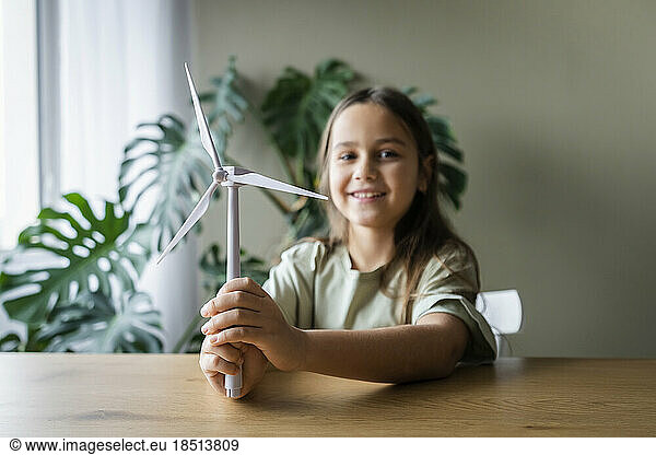 Girl holding wind turbine model on table at home