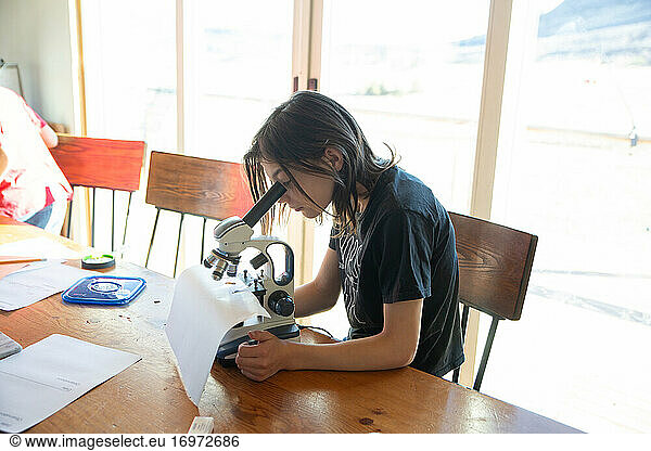Girl homeschooling looking under microscope