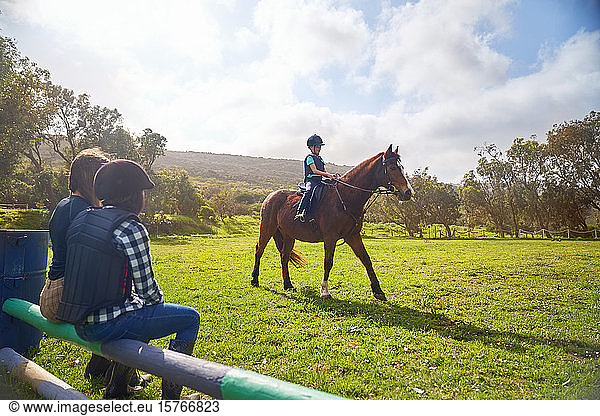 Girl horseback riding in sunny grass paddock