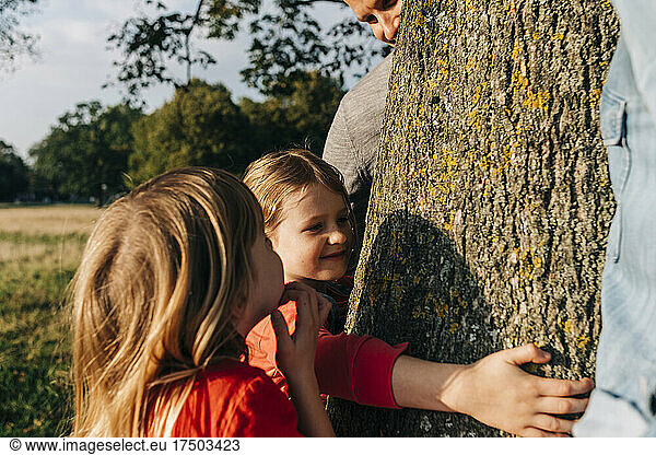 Girl hugging tree by parents and sister in park