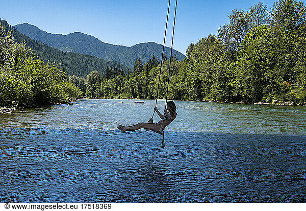 Girl in a bikini on a swing over a river in the mountains