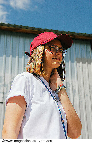 girl in a cap and glasses hold her hand on her neck
