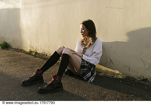 Girl in a short skirt sitting on the pavement in an alley