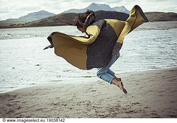 girl in beautiful cloak jumps on beach