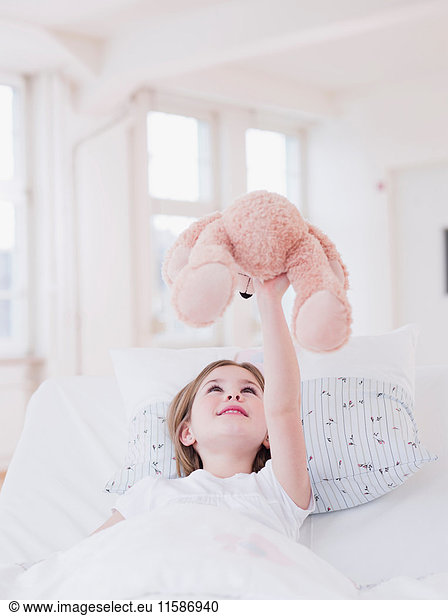 girl in bed playing with teddy bear