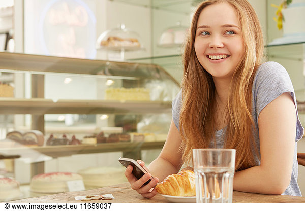 Girl in cafe holding smartphone smiling