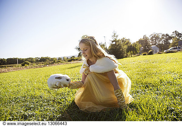 Girl in costume holding rabbit on field against clear sky