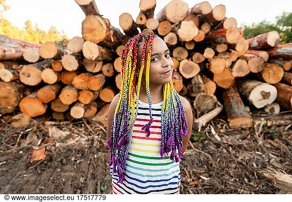 Girl in front of pile of logs glances at camera