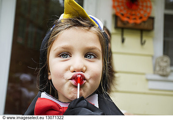 Girl in Halloween costume eating lollipop while standing against house