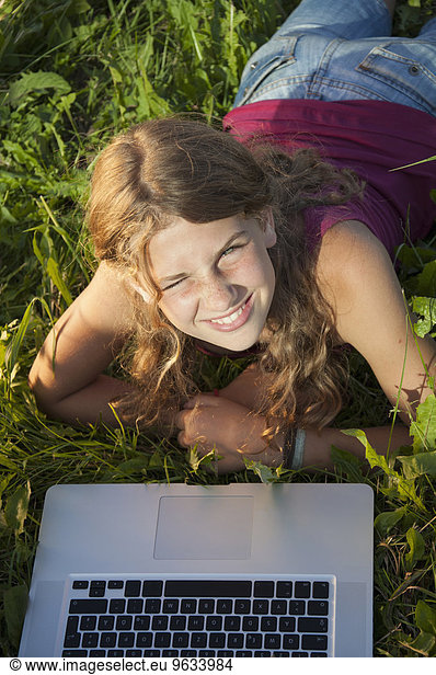 Girl (12-13) in meadow using laptop  elevated view