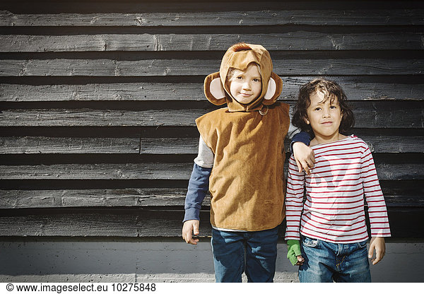 Girl in monkey suit standing with friend against black wooden wall