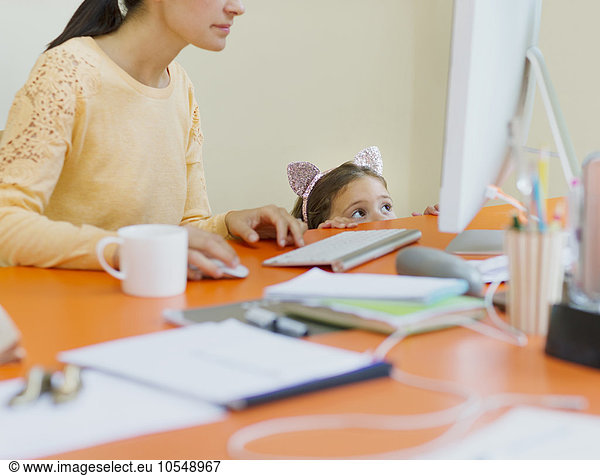 Girl in mouse ears headband watching mother work at computer