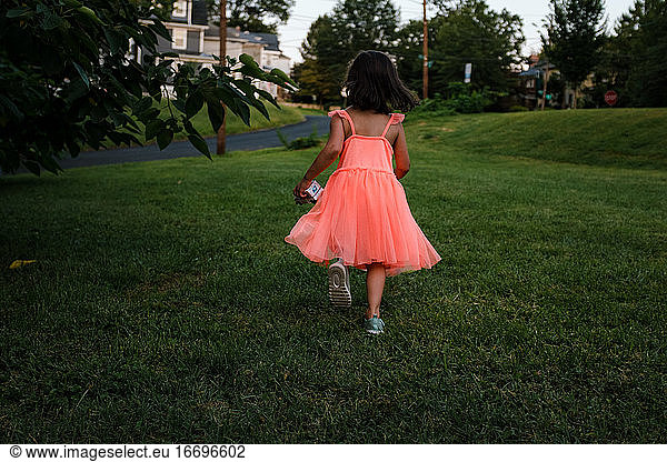 girl in orange dress holding toy truck running in grass