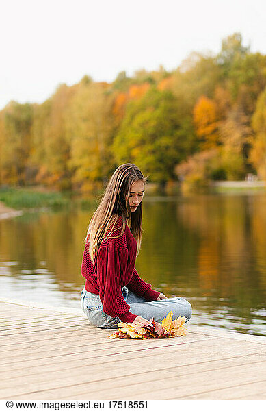 Girl in red sweatshirt sitting by the lake in autumn park