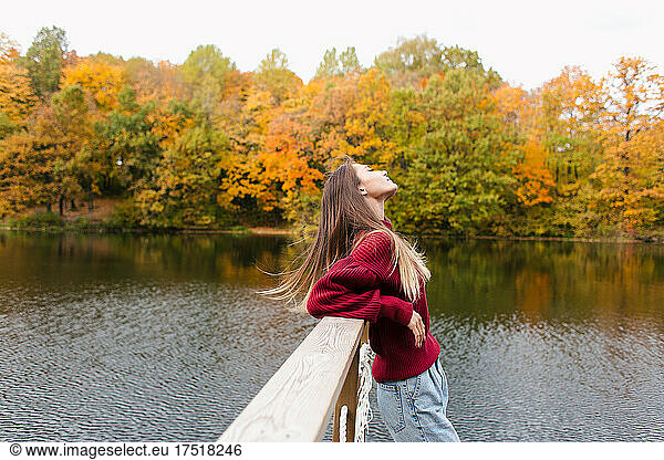 Girl in red sweatshirt standing by the lake in autumn park