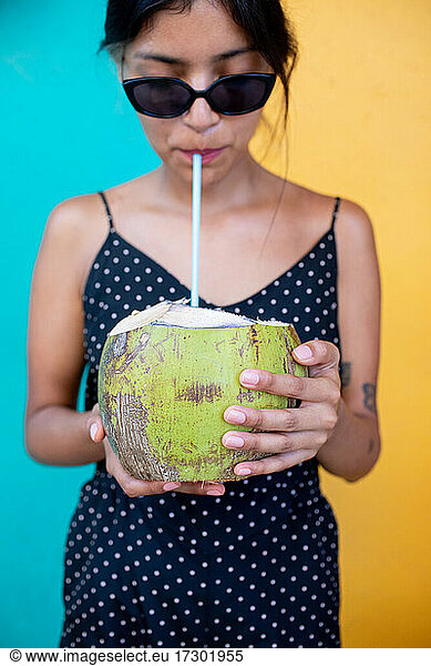 Girl in sunglasses drinking from coconut
