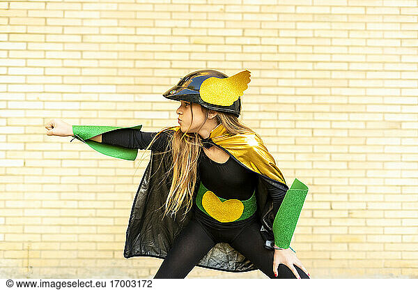 Girl in super heroine costume posing at brick wall
