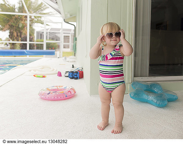 Girl in swimwear wearing heart shape sunglasses while standing at poolside