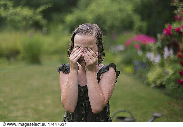 Girl in the rain wipes her eyes in her garden.