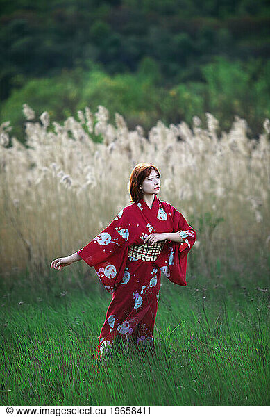 girl in white makeup red kimono stands against a background of reeds