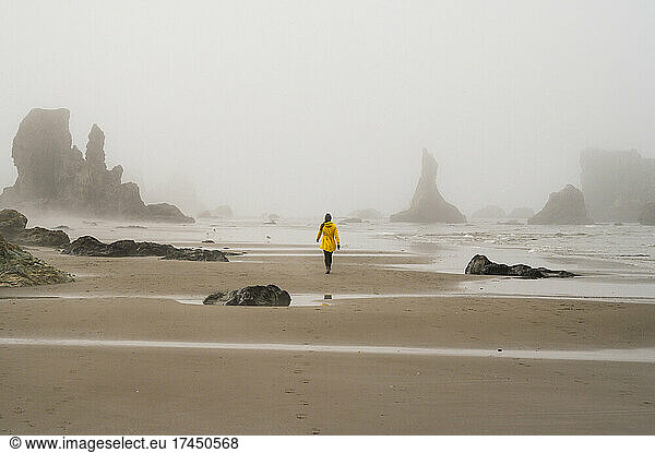 Girl in yellow rain jacket walking on foggy oregon beach