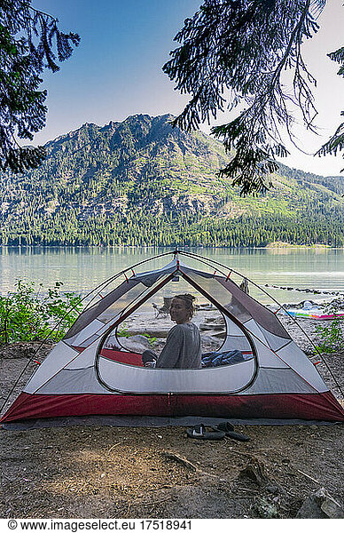 Girl inside a tent smiling at camera next to a mountain lake